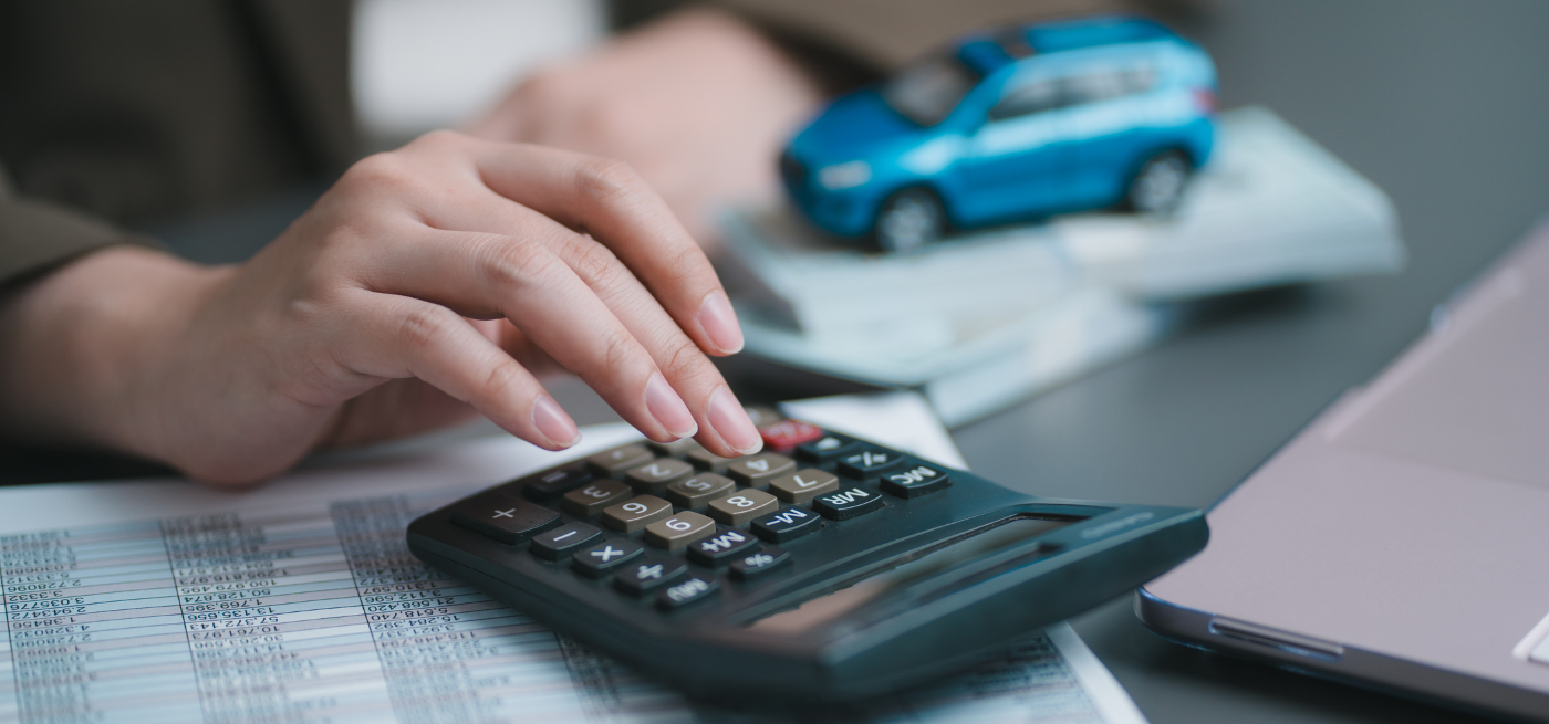 Pessoa a usar calculadora com carro em miniatura e documentos ao fundo